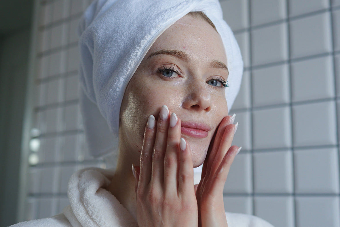 Frau mit Handtuch im Haar trägt Gesichtscreme auf – Skincare-Routine ab 40