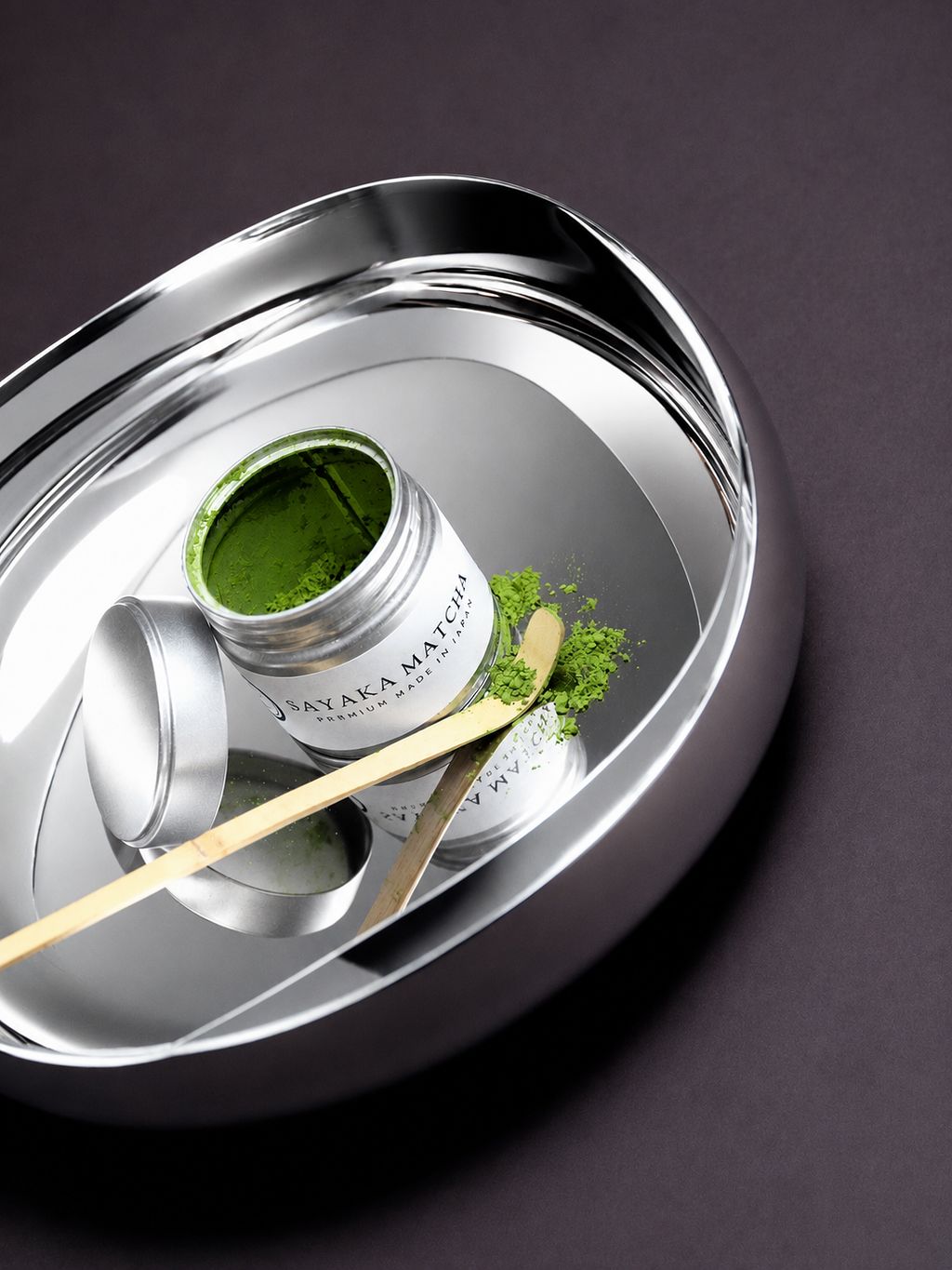 Geöffnete Dose Sayaka Premium Matcha Pulver mit Bambuslöffel auf einem Edelstahltablett